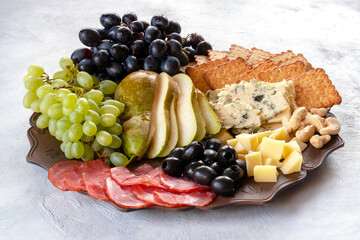 Plate with parmesan, gorgonzola, blue and green grapes, pears, olives, smoked sausage, cashews and crackers. Snack board.