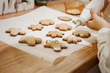 Fototapeta na wymiar Cooking Christmas gingerbread. Child decorating freshly baked cookies with icing and confectionery mastic, view from above. Festive food, family culinary, Christmas and New Year traditions concept. 