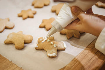 Cooking Christmas gingerbread. Child decorating freshly baked cookies with icing and confectionery mastic, view from above. Festive food, family culinary, Christmas and New Year traditions concept. 