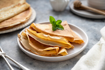 Golden crepes with jam and honey, on grey background.