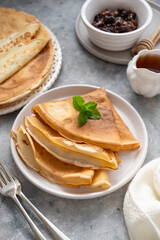 Golden crepes with jam and honey, on grey background.