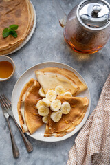 Crepes or thin pancakes, served with honey and cup of tea, on grey background.