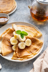 Crepes or thin pancakes, served with honey and cup of tea, on grey background.