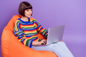 Photo of calm focused remote worker lady sit beanbag typing pc wear striped sweater isolated purple color background