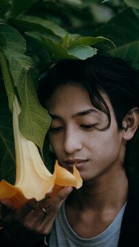Vertical shot of a young handsome Indonesian man posing in nature with leaves and a flower