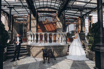 the groom in a black suit and the bride in a white dress stand at the entrance to the palace