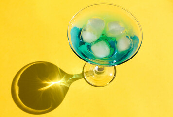 Blue cocktail with ice and on a yellow background, top view, hard shadows, summer holiday concept