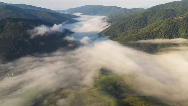 Aerial view on amazing flowing morning fog spreads over green meadows in autumn mountains. Ukrainian Carpathian mountains. UHD 4k video