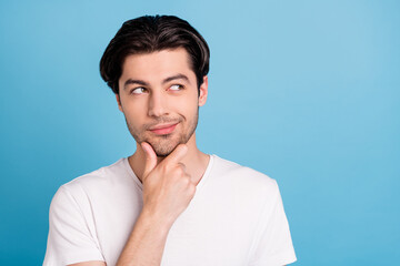 Photo of minded pensive guy look empty space finger chin think wear white t-shirt isolated blue...