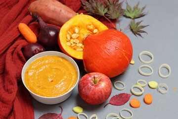 Creamy squash soup, pumpkin, apple, baby carrots, leek and red onion on a table. Top view photo of autumn food. Balanced diet concept. 