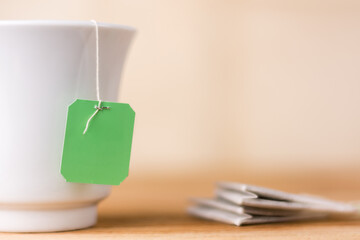 tea bag with a green label in a ceramic white cup on a table top, warm yellow background, closeup...