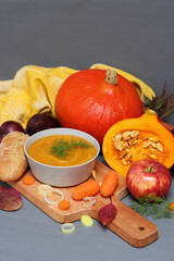 Bowl of hot pumpkin soup, seasonal vegetables and fruits on a table. Vegetarian meal close up. Healthy eating concept. 