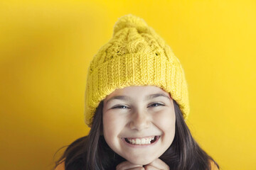 Happy beautiful smiling child girl in knitted hat on yellow background Space for text. Yellow colour consept. Spase for text.