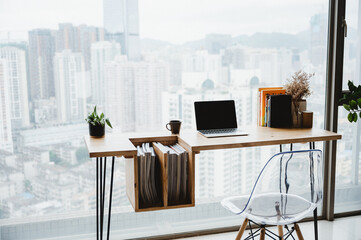 Light apartment interior with minimalist workplace and transparent chair and table with laptop and books on a white marble concrete floor near window with a city view
