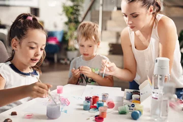 Rolgordijnen Young mom and her kids having fun and painting at home © konradbak