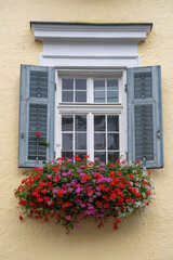 Fototapeta na wymiar Beige plaster facade of a mountain house and windows with colorful flowers in Austria