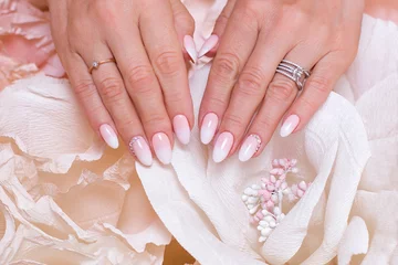 Foto op Canvas  Female hands with ombre manicure nails, pink gel polish, on paper flowers background © Galina