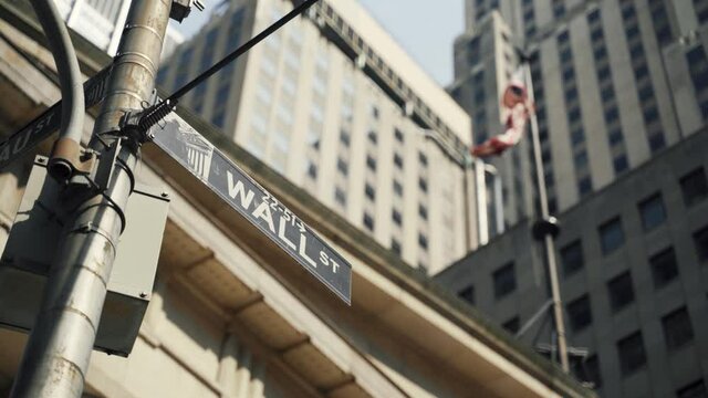 Wall Street sign with American flags in the background, shot in the heart of the business world in Manhattan. Business, finance, worldwide stock trade and economics concept.