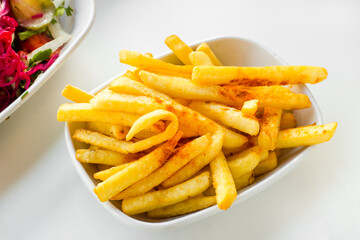 Fried french fries with paprika spice on oval plate on the white table