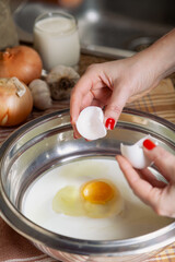 Female hands hold two halves of egg shell over bowl..
