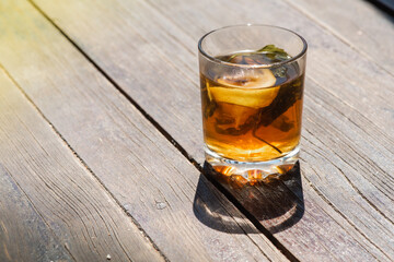 glass cup with tea, lemon and mint on a gray-brown wooden surface, light shadow, sunlight of morning tea, top view, isolated on wooden background 