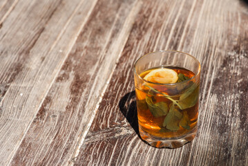 glass cup with tea, lemon and mint on a gray-brown wooden surface, light shadow, sunlight of morning tea, top view, isolated on wooden background 
