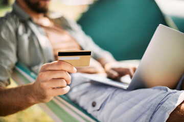 Fototapeta premium Close-up of man uses credit card and laptop while e-banking in nature.