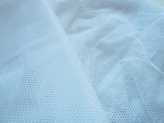 Sheer white net-like tulle. Mesh fabric is wrinkled or folded carelessly. Close-up. White - blue...