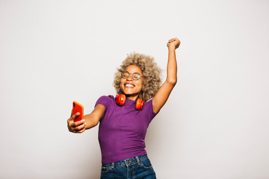 Portrait of Smiling Young woman using smart phone and headphones dancing Against White Background