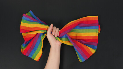 Hand is holding rainbow handkerchief on black background.