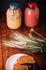 Two jars of homemade kvass, bread and hibiscus kvas, wheat ears, slices of bread on wooden dark rustic background. Ukrainian summer drink