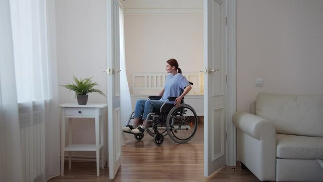 A young disabled woman is riding in her wheelchair around the room and stretching 