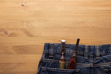 Chisel woodwork tool in jeans pocket at wooden table background. Woodworking concept