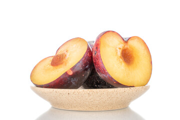 Two halves of juicy purple plums on a ceramic saucer, close-up, isolated on white.