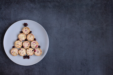 Cute edible Christmas tree made of cookies on a round plate on a grey dark background. Creative tree. Space for design and text. Concept holidays, pastries, New Year