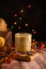 Pumpkin latte on a dark background with pumpkins and autumn leaves and colored lights. Autumn composition in warm colors