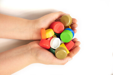 Multi-colored screw caps for plastic bottles in the hands of a child, ecology