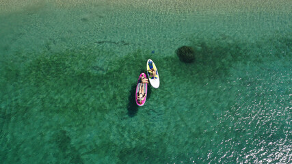 Aerial drone photo of fit women sit on Stand Up Paddle or SUP in tropical exotic island shallow water emerald bay