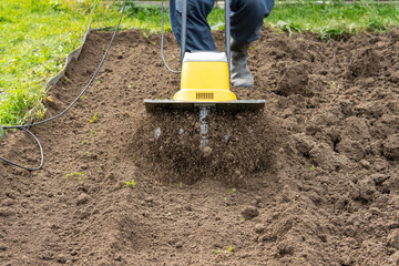 Loosening the soil in the garden beds with an electric hand-held cultivator - obrazy, fototapety, plakaty