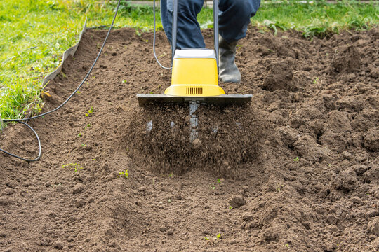Loosening the soil in the garden beds with an electric hand-held cultivator