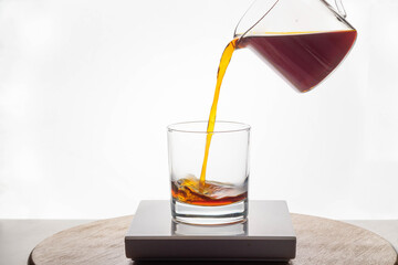 Coffee being poured into clear tumbler against bright backlight