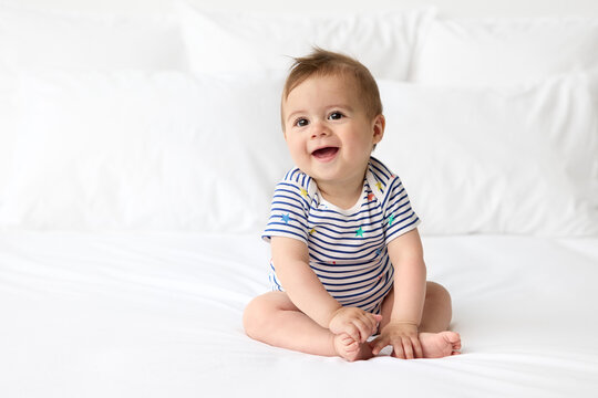 Cute smiling baby sitting on white bed