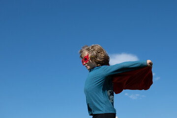Little kid boy plays superhero. Child on the background on sky.