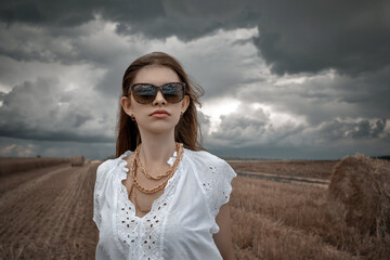 a woman in big glasses and a white blouse in an autumn field dramatic sky in clouds