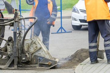Repair of city roads and replacement of worn asphalt concrete pavement. A worker with a shovel throws concrete into a pit to eliminate damage to the roadway.