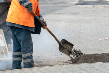 Repair of city roads and replacement of worn asphalt concrete pavement. A worker with a shovel throws concrete into a pit to eliminate damage to the roadway.