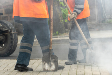 A group of road service workers is laying new asphalt in the city. Repair of asphalt on roads, autobahns and highways. Steam from the new asphalt concrete mix.