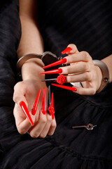 Close-up of female arms and long legs. The girl is holding a crown in her hands. Red nails on a dark background.