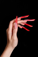 Close-up of female arms and long legs. The girl is holding a crown in her hands. Red nails on a dark background.