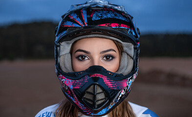 a beautiful girl with big eyes in a helmet looks at the camera against a background of blue sky, forest and sand